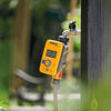 Yellow digital garden hose timer attached to outdoor faucet in a green garden setting