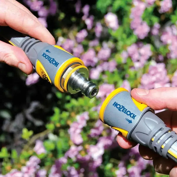 Two hands holding Hozelock garden nozzles against a blurred floral background