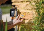 Person replacing irrigation timer batteries on a stone wall outdoors