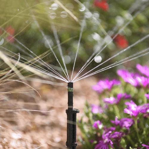 Sprinkler spraying water in a garden with flowers and plants in the background