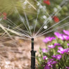 Sprinkler spraying water in a garden with flowers and grass in the background