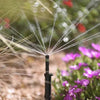 Sprinkler spraying water in a garden with flowers and grass in the background