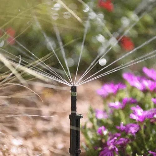 Sprinkler spraying water in a garden with flowers and grass in the background