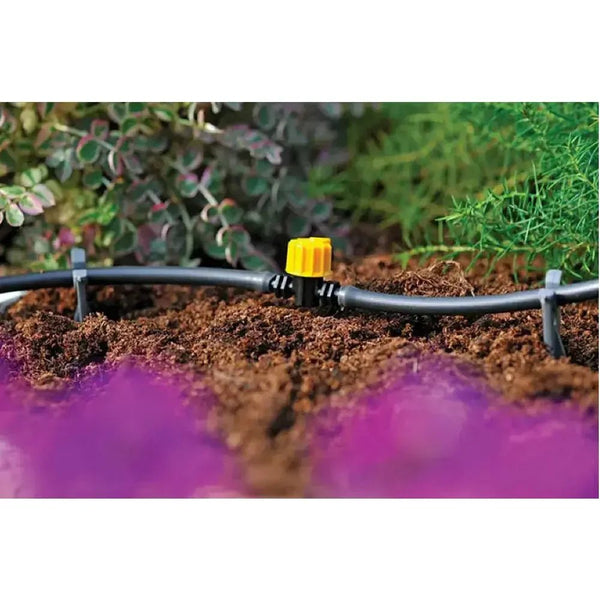 Garden irrigation system with a yellow valve in soil, surrounded by plants.