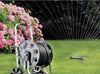 Claber Gemini 8994 Garden hose reel with sprinkler spraying water on grass next to pink flowers
