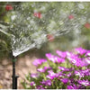 Sprinkler watering plants with a blurred background of flowers and greenery