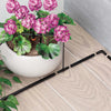 Potted plant with pink flowers on a wooden floor next to black plant support stakes.