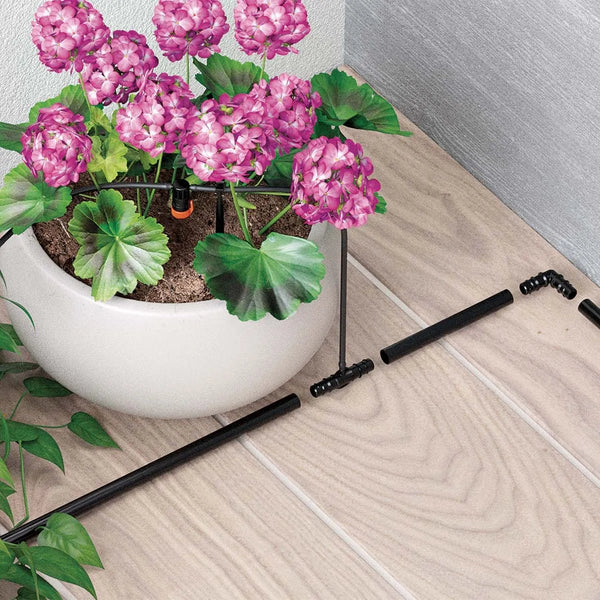 Potted plant with pink flowers on a wooden floor next to black plant support stakes.