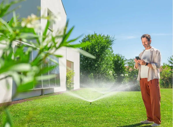 Person using a smartphone while standing in a garden with a sprinkler system