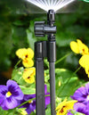 Sprinkler head on a stand with flowers in the background