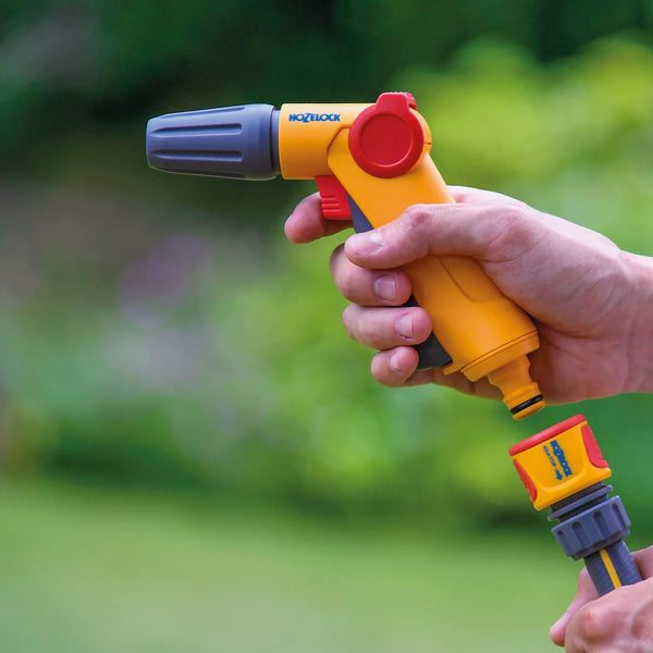 Hand holding a yellow and red garden hose nozzle with a blurred green background