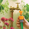 Hand holding a green garden hose with a yellow connector attached to a brass outdoor faucet.