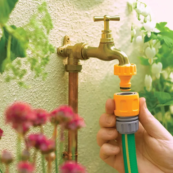 Hand holding a green garden hose with a yellow connector attached to a brass outdoor faucet.