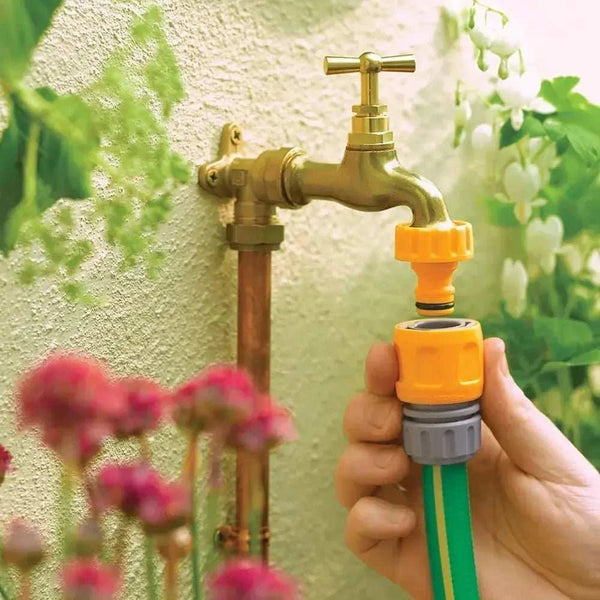 Hand holding a green garden hose with a yellow connector attached to a brass outdoor faucet.