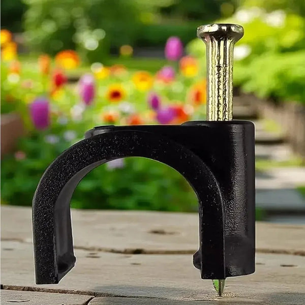 Black metal clip holding a nail on a wooden surface with a garden background