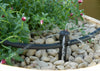 Small irrigation sprinkler with pebbles and plants in a container garden setting