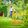 Woman watering garden with yellow Tricoflex hose on green lawn and colorful flowers