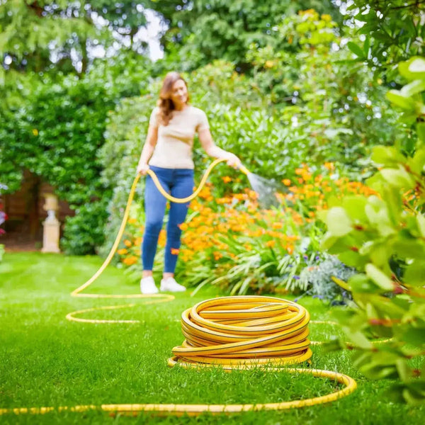 Woman watering garden with yellow Tricoflex hose on green lawn and colorful flowers