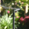 Sprinkler spraying water in a garden with blurred greenery and flowers in the background