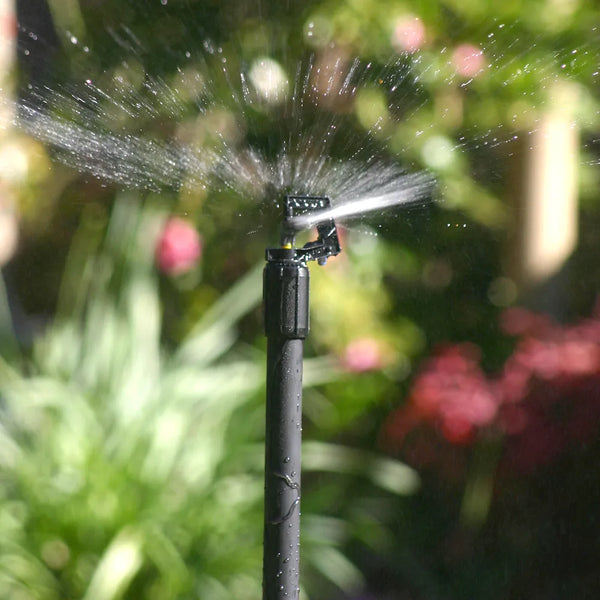 Sprinkler spraying water in a garden with blurred greenery and flowers in the background