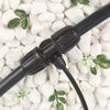 Black garden hose with connectors on a background of white pebbles and small green plants