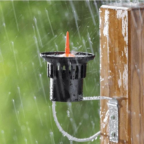 Black irrigation valve with an orange cap attached to a wooden post, raining in the background