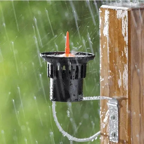 Black irrigation valve with an orange cap attached to a wooden post, raining in the background