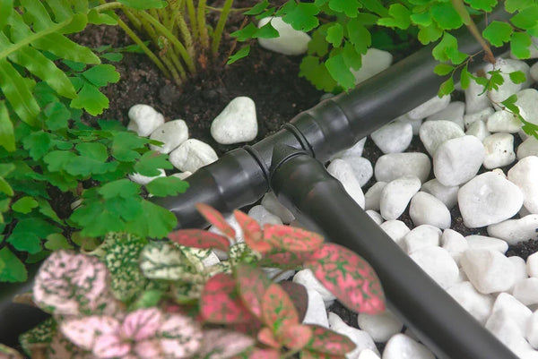 Black irrigation fitting on pebbles with green plants