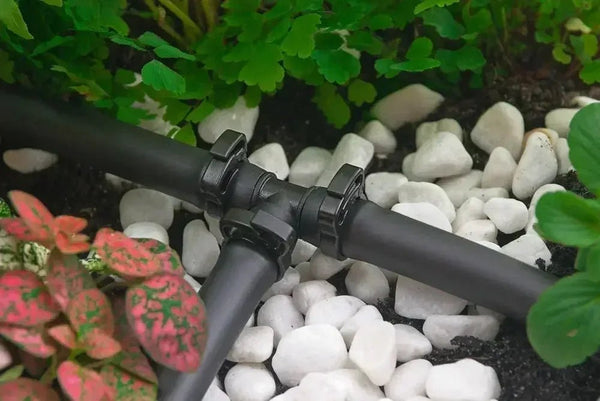 Black garden hose with a connector on pebbles and plants