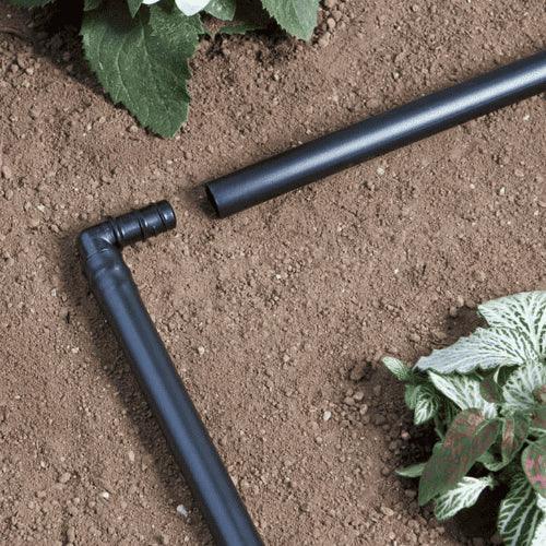 Black garden irrigation pipes on soil with plants around