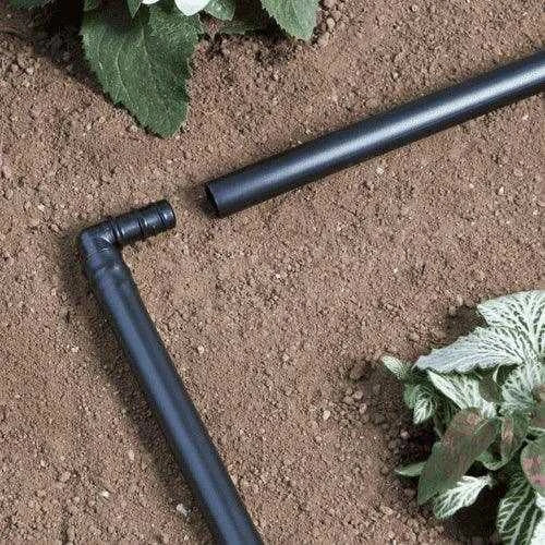 Black garden irrigation pipes on soil with plants around