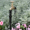 Brass garden faucet with black hose on a background of green foliage and pink flowers