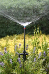 Sprinkler spraying water in a garden with greenery and flowers in the background