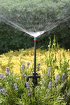 Sprinkler spraying water in a garden with greenery and flowers in the background