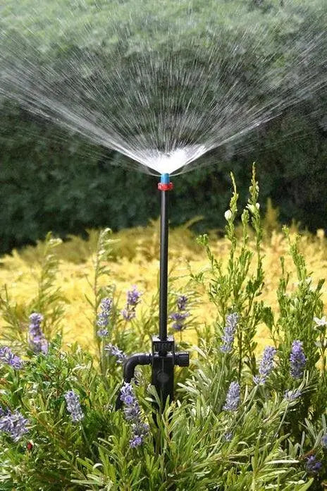 Sprinkler spraying water in a garden with greenery and flowers in the background