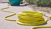 Coiled yellow garden hose on a concrete surface with a blue ball in the background.