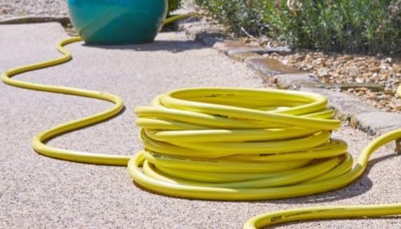 Coiled yellow garden hose on a concrete surface with a blue ball in the background.