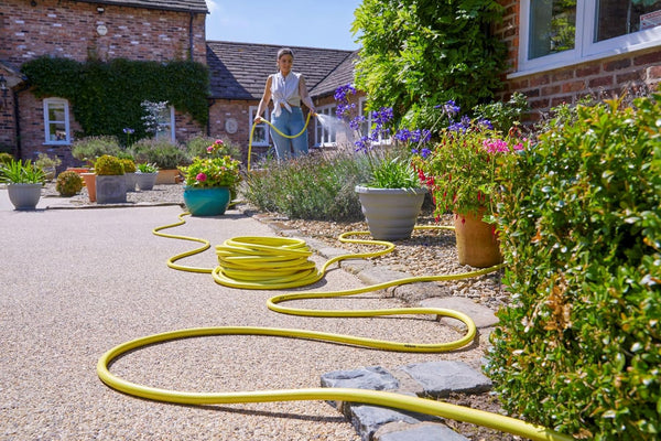 Person watering plants with a yellow hose in a garden setting.