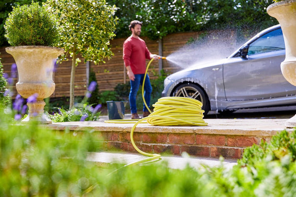 Man washing a car with a garden hose in a garden setting