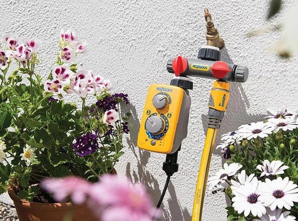 Gardening tool with yellow handle and red accents on a white wall with flowers in the foreground