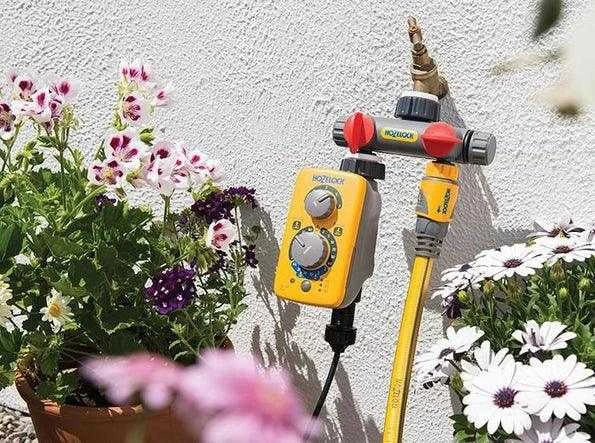Gardening tool with yellow handle and red accents on a white wall with flowers in the foreground