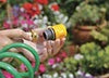 Green garden hose with a yellow nozzle on a blurred background of plants