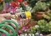 Green garden hose with a yellow nozzle on a blurred background of plants