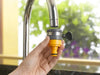 Hand holding a yellow and black faucet adapter against a blurred outdoor background