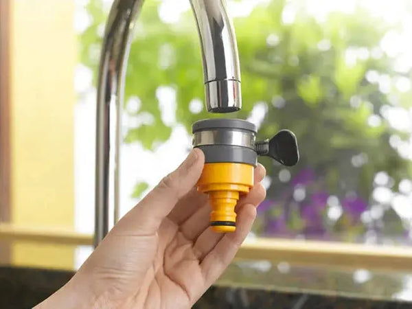 Hand holding a yellow and black faucet adapter against a blurred outdoor background