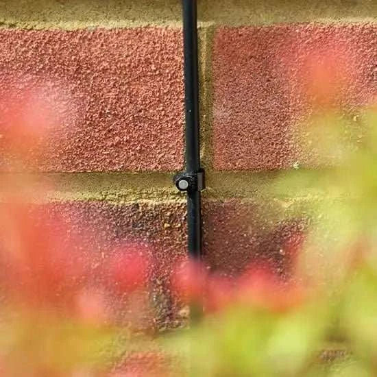 Black cable running along a red brick wall with blurred flowers in the foreground