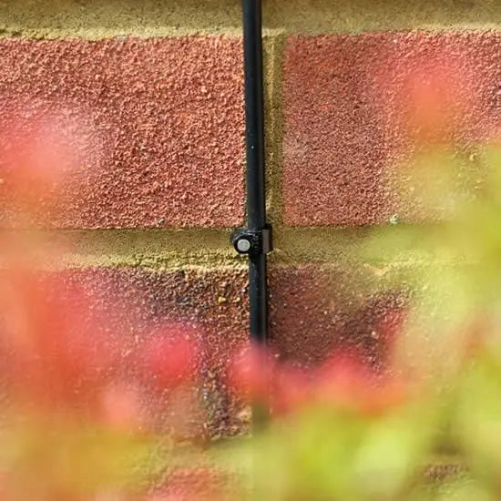 Black cable running along a red brick wall with blurred flowers in the foreground