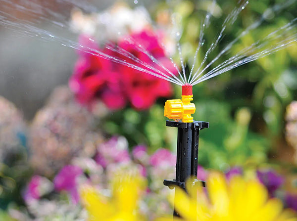 Hozelock Sprinkler spraying water in a garden with flowers in the background