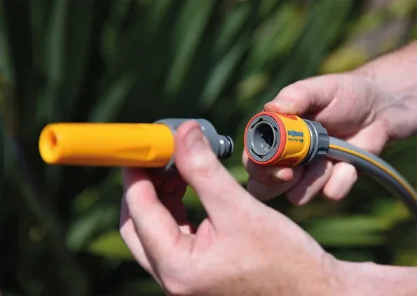 Person holding two garden hose nozzles against a blurred green background