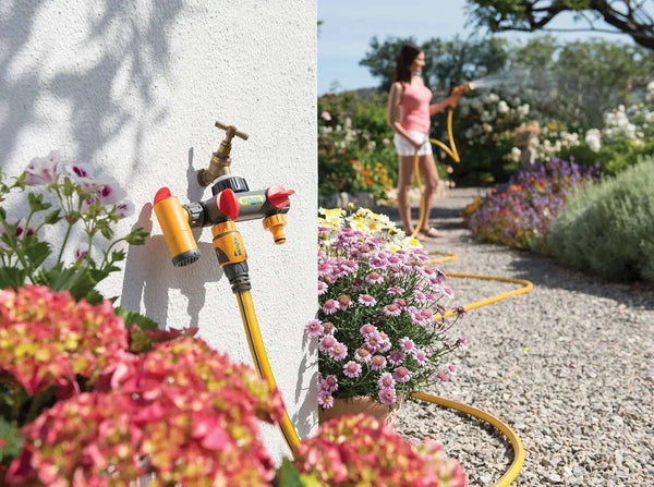 Hose and nozzle with flowers and a person watering plants in a garden.